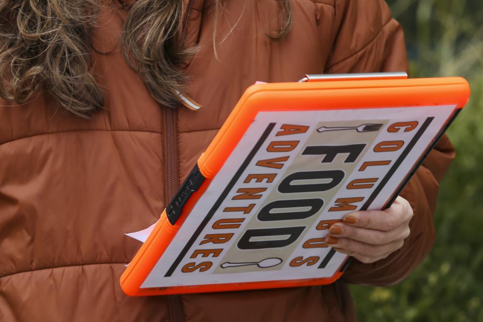 A guide with Columbus Food Adventures holds a clipboard while speaking to participants about the history of Columbus and the Short North during a tour.