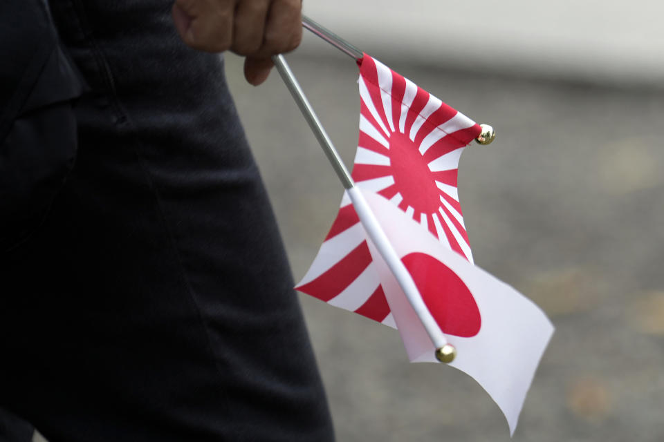 A visitor holds small Japanese flag and a rising sun flag at the Yasukuni Shrine, which honors Japan's war dead, Tuesday, Aug. 15, 2023, in Tokyo. Japan holds annual memorial service for the war dead as the country marks the 78th anniversary of its defeat in the World War II. (AP Photo/Eugene Hoshiko)