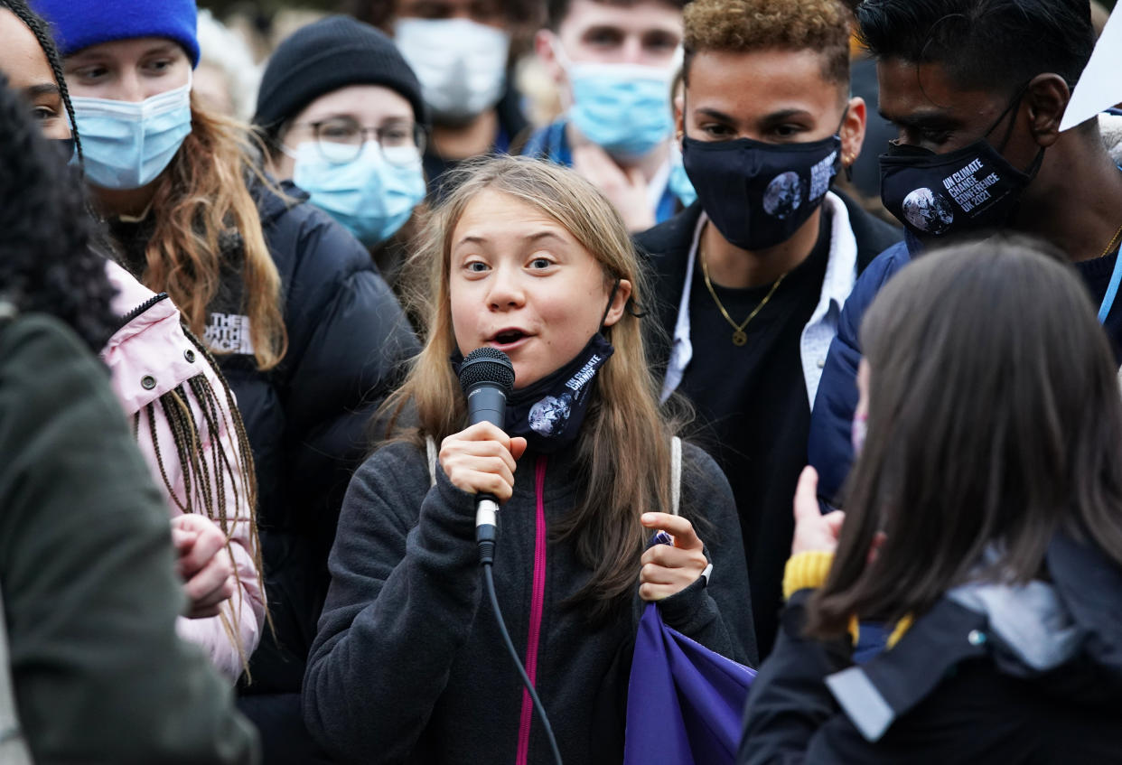 Greta Thunberg speaks into a microphone while standing alongside climate activists wearing coats, hats and face masks.