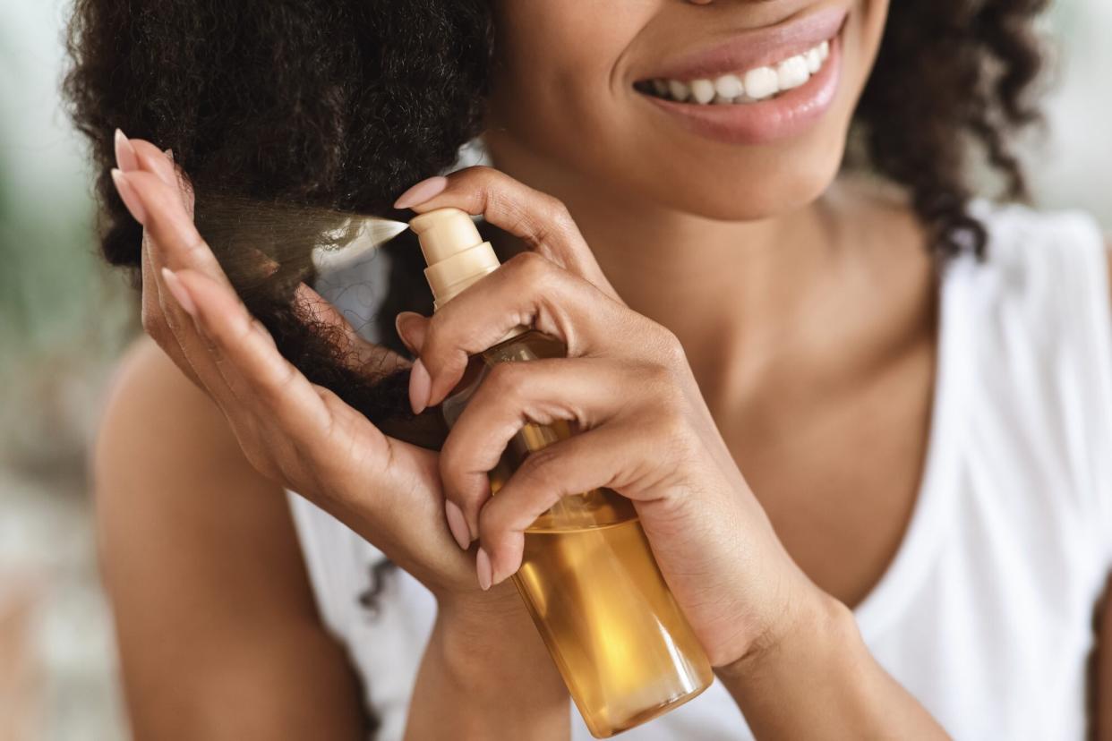 Smiling Woman Spraying Essential Oil On Curly Hair