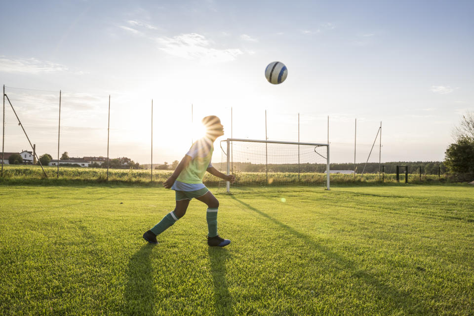 Young football player heading the ball on football ground at sunset