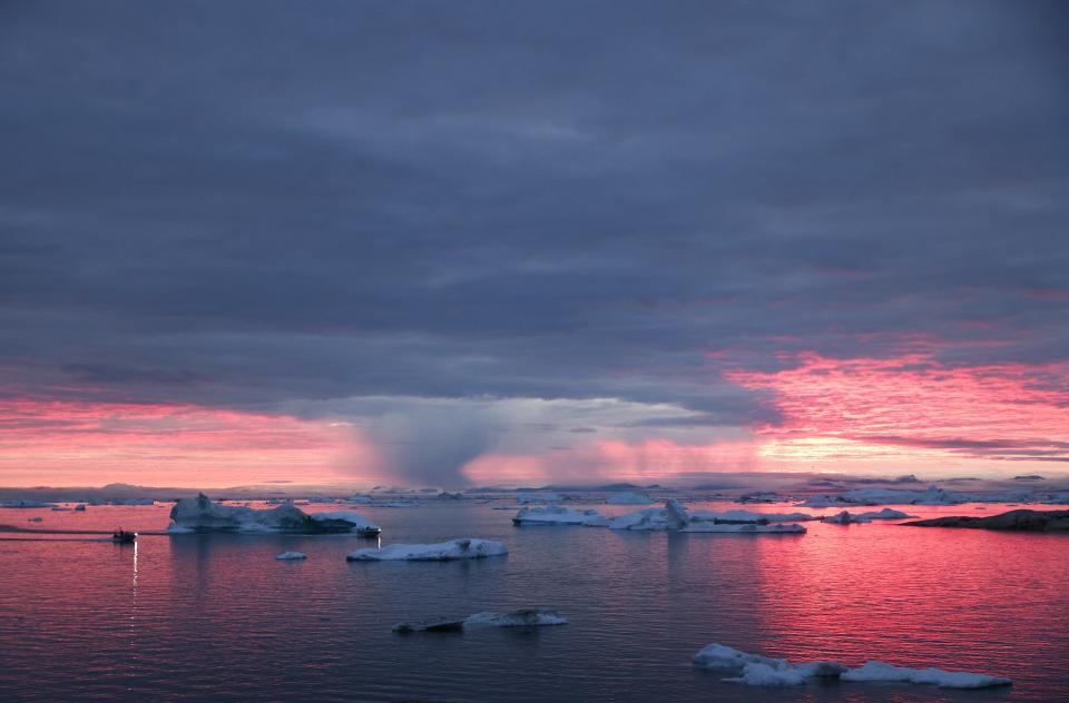 The sun sets as rain falls beyond floating ice and icebergs in Disko Bay above the Arctic Circle on Sept. 4, 2021, in Ilulissat, Greenland.