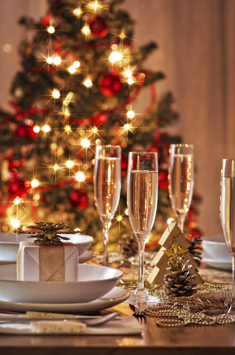 A decorated christmas dining table with champagne glasses and christmas tree in background