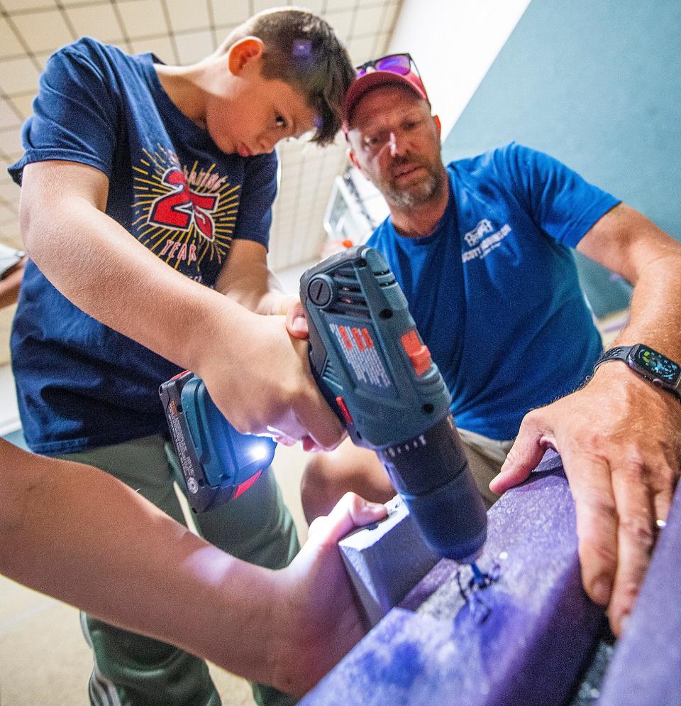 Under the direction of Scott Robinson, right, Isaac Eason drills in a screw as they assemble buddy benches at Clear Creek Christian School on Friday, May 12, 2023.