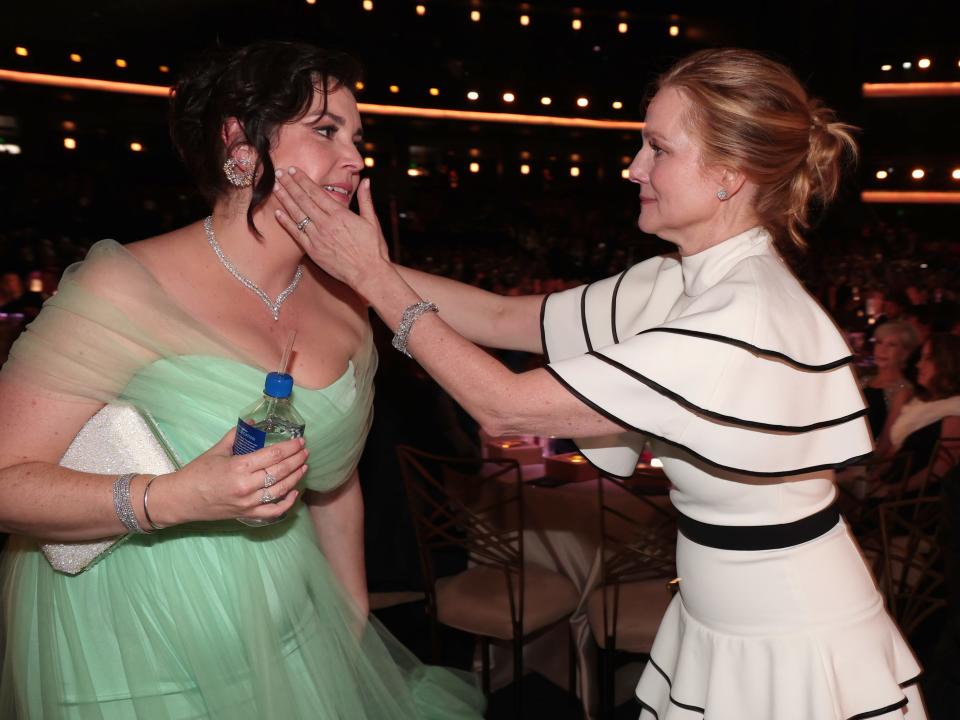 laura linney, right in a white and black dress, cradles melanie lynskey, right in a mint colored dress, face as they smile