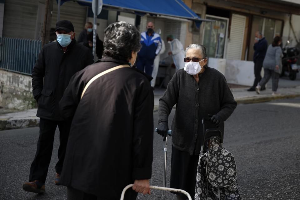 An elderly woman wearing a face mask against the spread of coronavirus, speaks with another woman, in Athens, Monday, Nov. 23, 2020. Greece has seen a major resurgence of the virus after the summer, leading to dozens of deaths each day and thousands of new infections. (AP Photo/Thanassis Stavrakis)