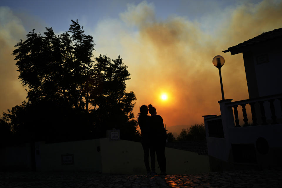 Two women watch a wildfire burning near houses in Alcabideche, outside Lisbon, Tuesday, July 25, 2023. Hundreds of firefighters and over a dozen airplanes were fighting a wildfire that spread quickly fanned by strong winds. (AP Photo/Armando Franca)