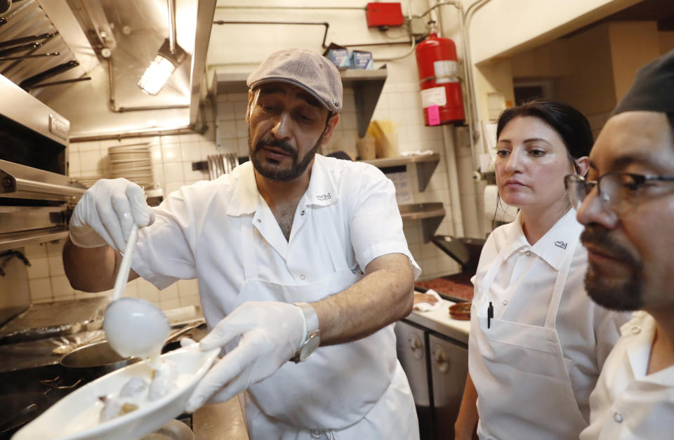 In this June 18, 2019, photo, chef Diaa Alhanoun, left, pours yoghurt sauce over kibbeh, a traditional Mediterranean recipe containing seasoned ground beef or lamb dumplings, as chefs Lauren Radel, center, and Alfredo Medel watch in the kitchen at Porsena, while preparing for the 2019 Refugee Food Festival in New York. The goal of the global food festival, held once a year in major cities, hopes to call attention to refugee chefs and their culinary talents, raise awareness about the refugee cause, and encourage refugee integration in their host countries. (AP Photo/Kathy Willens)