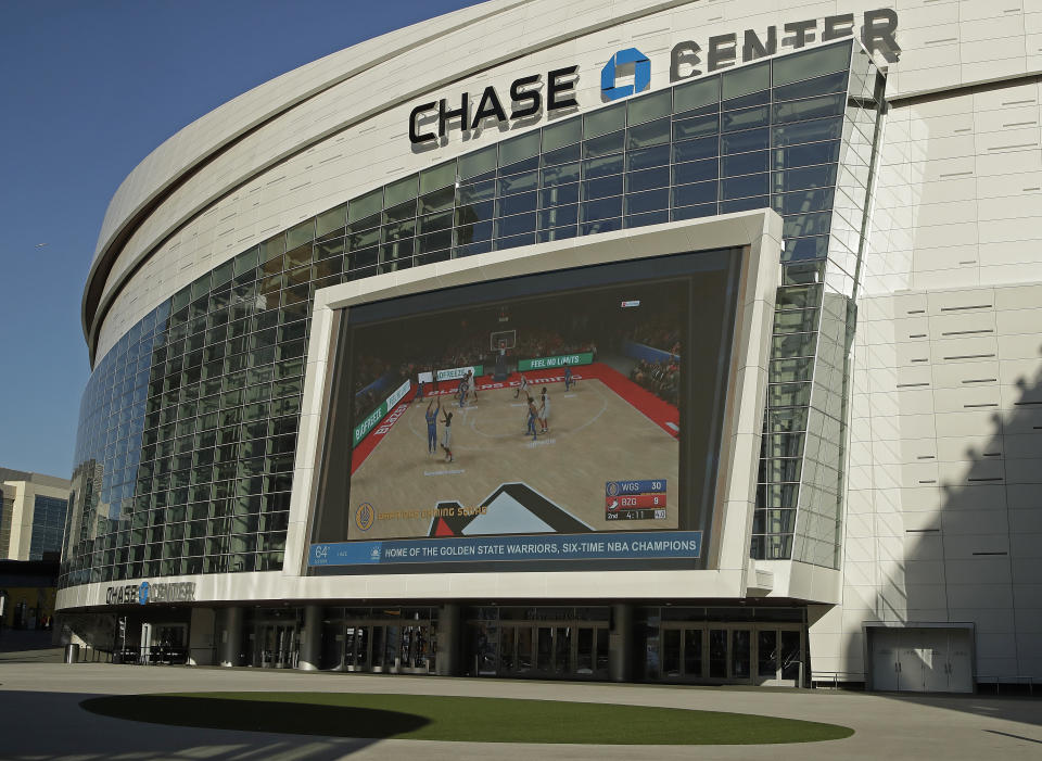 The Chase Center, home of NBA basketball's Golden State Warriors, show a pre-recorded video of a basketball game on a large screen at the entrance to the areana on a day the team was to play the Brooklyn Nets, Thursday, March 12, 2020, in San Francisco. The NBA suspended its season after a Utah Jazz player tested positive Wednesday for the coronavirus. (AP Photo/Ben Margot)