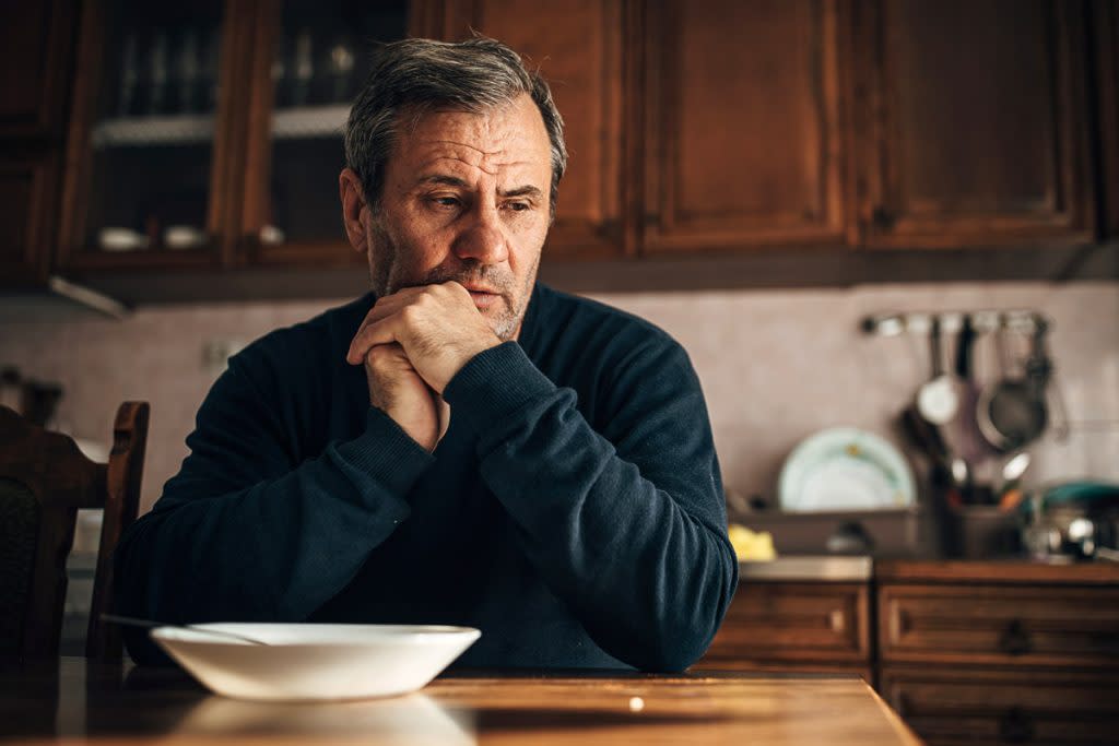 A senior citizen looks stressed out while sitting at his kitchen table.