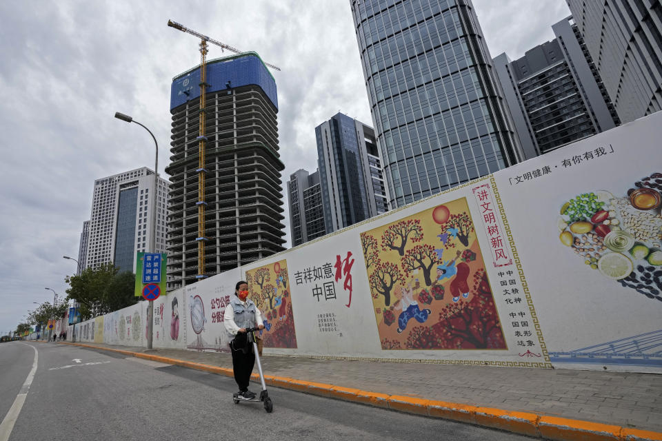 A girl wearing a face mask to help protect from the coronavirus rides a scooter past Chinese government's propaganda "China Dream" billboard on display along a commercial office buildings under construction in Tongzhou, outskirts of Beijing, Monday, Oct. 4, 2021. China’s economy is losing steam as President Xi Jinping's government cracks down on corporate debt and energy use in pursuit of more stable, sustainable growth. (AP Photo/Andy Wong)