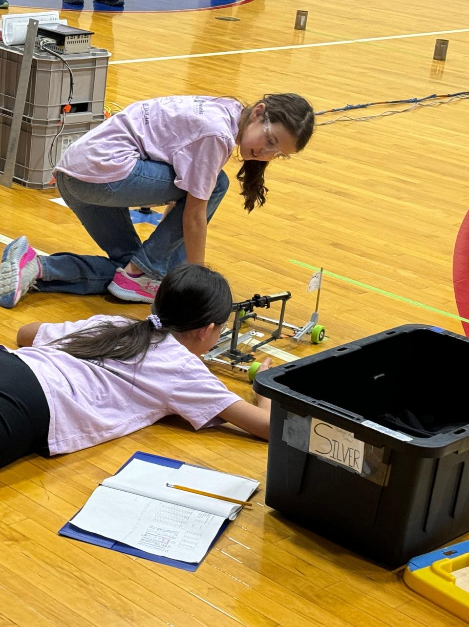 Pictured are Mia Teusan and Jessie Cheng as they align their Wheeled Vehicle, for which they earned 2nd place at the Kenston Invitational. The vehicle they built traveled 9 meters, around cans, stopping 1.6 centimeters from the target.