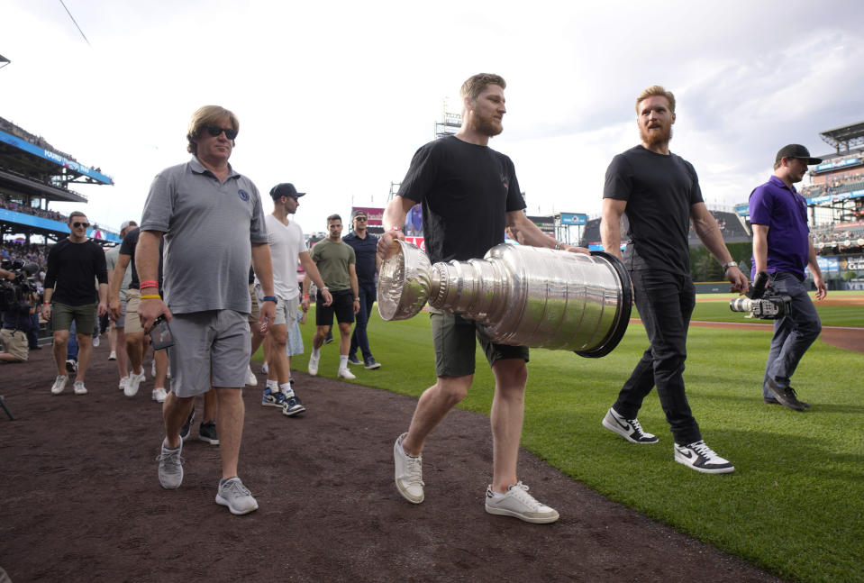 Colorado Avalanche captain Gabriel Landeskog, second from right, walks next to Nathan MacKinnon, who carries the Stanley Cup as the NHL hockey team is honored by the Colorado Rockies before the baseball team's game against the Los Angeles Dodgers on Wednesday, June 29, 2022, in Denver. (AP Photo/David Zalubowski)