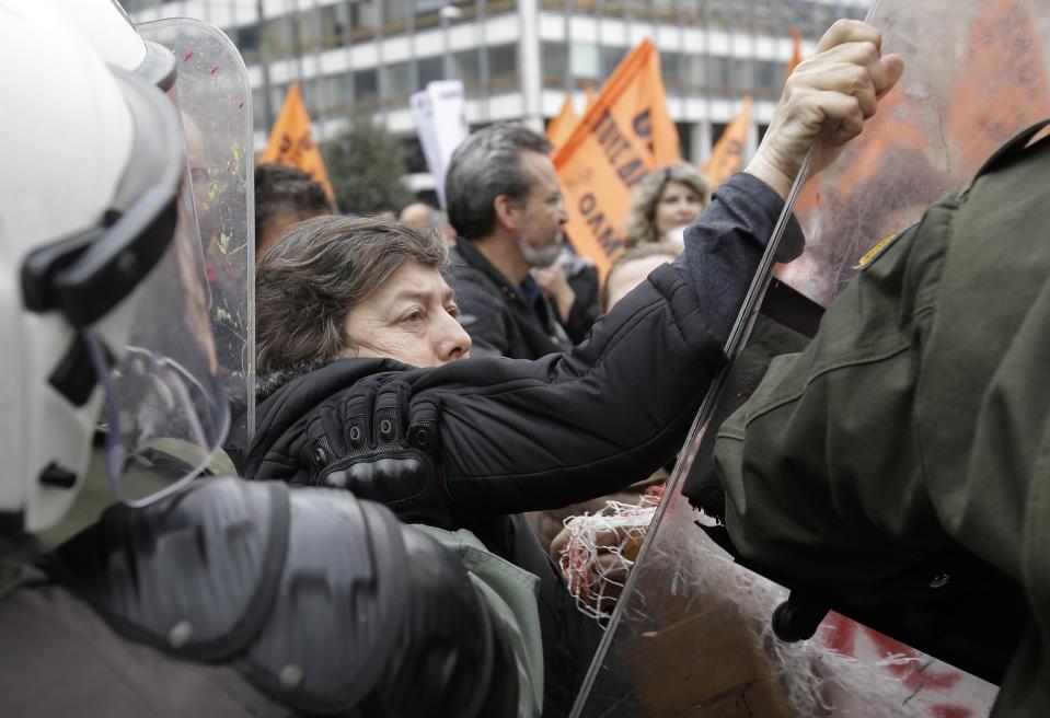 A protesting woman holds the shield of a riot policeman as another one pushes her, outside the Finance Ministry during a rally in Athens, on Friday, Feb. 28, 2014. Some hundreds of teachers, municipality workers, school guards and cleaning women who have been suspended on reduced pay pending transfer to other public sector jobs or dismissal, took part in the protest as the officials from the European Union, European Central Bank and International Monetary Fund, together known as the troika, were holding talks with the Minister of Administration Reform Kyriakos Mitsotakis and other government officials. (AP Photo/Thanassis Stavrakis)