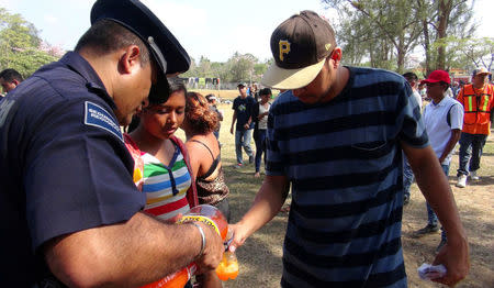 A policeman pours soft drink for a Central American migrant participating in a caravan heading to the U.S. in Matias Romero, Oaxaca, Mexico, April 2, 2018. REUTERS/Jose de Jesus Cortes