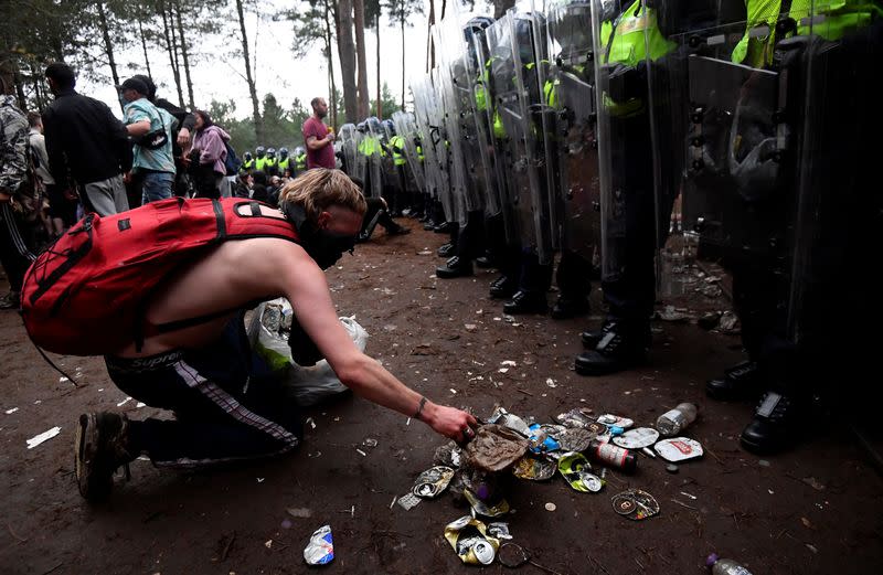 A reveller clears up a rubbish in front of riot police at the scene of a suspected illegal rave in Thetford Forest