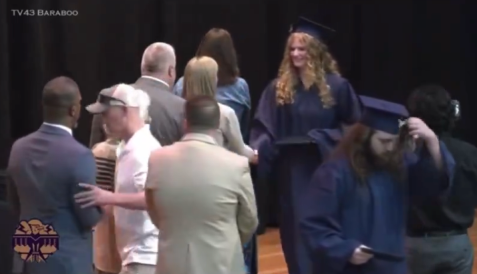 An unnamed father of a graduate pictured shoving Superintendent Rainey Briggs (far left) off the stage. In 2018, the same high school made national news after a photo emerged of several students performing the Nazi salute (TV43 Baraboo)