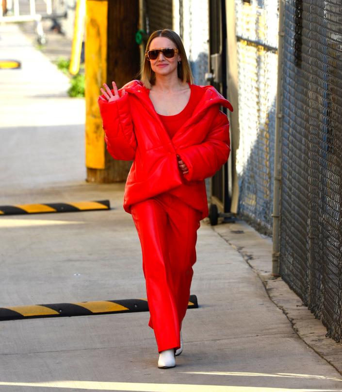 Kristen Bell in an all-red outfit walking down the street and waving