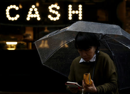 FILE PHOTO: A pedestrian holding an umbrella and her wallet walks past the word "CASH", part of a sign on a street at a shopping district in Tokyo, Japan, March 7, 2016. REUTERS/Yuya Shino/File Photo