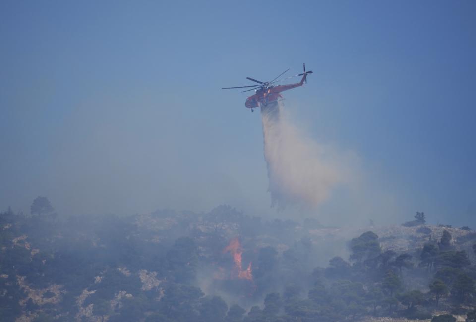 A helicopter drops water over a wildfire atop Mount Parnitha, in northwestern Athens, Greece, Thursday, Aug. 24, 2023. A major wildfire burning on the northwestern fringes of the Greek capital has torched homes and is now threatening the heart of a national park of Parnitha, one of the last green areas near the Greek capital. (AP Photo/Thanassis Stavrakis)