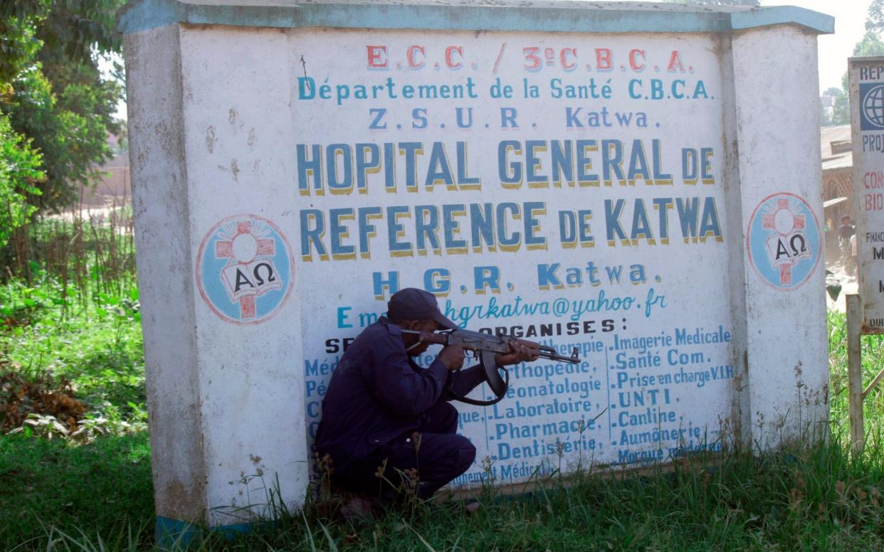 Police shelter behind a sign as they guard Butembo University Hospital, where a doctor was killed on Friday - AP