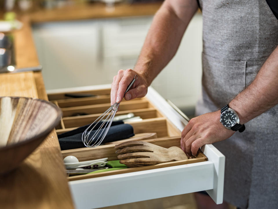 Someone putting items into the utensils drawer.