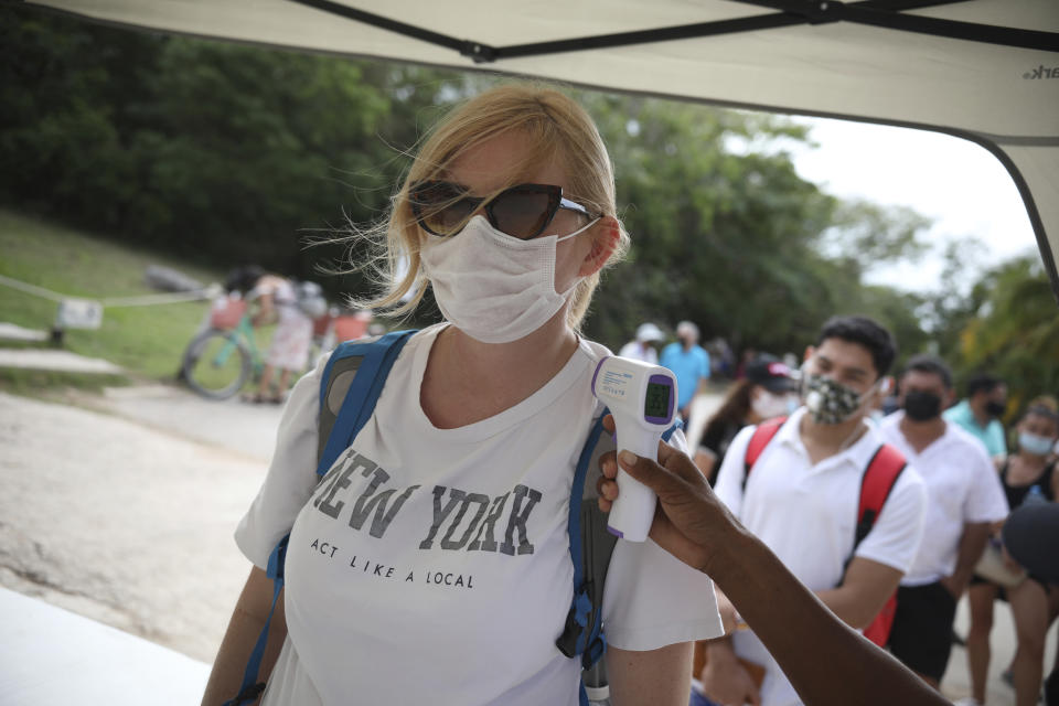 A tourist, wearing a protective face mask, stands still as an employee measures her body temperature as a preventive measure amid the new coronavirus pandemic, upon her arrival to the Mayan ruins in Tulum, Quintana Roo state, Mexico, Tuesday, Jan. 5, 2021.(AP Photo/Emilio Espejel)