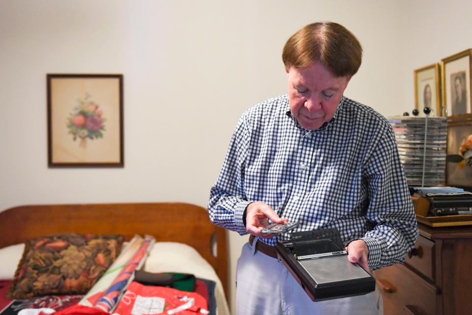 Lee Alexander, local radio host for 53 years, looks at a tape and tape player, one of the many forms technology took to play music in his decades of experience as a radio host, in his home in Greenville, SC, on Monday, Oct. 30, 2023.