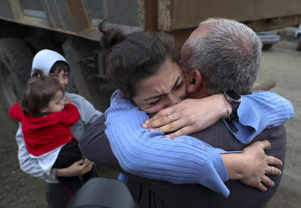 Two people embrace next to a child carrying a toddler.