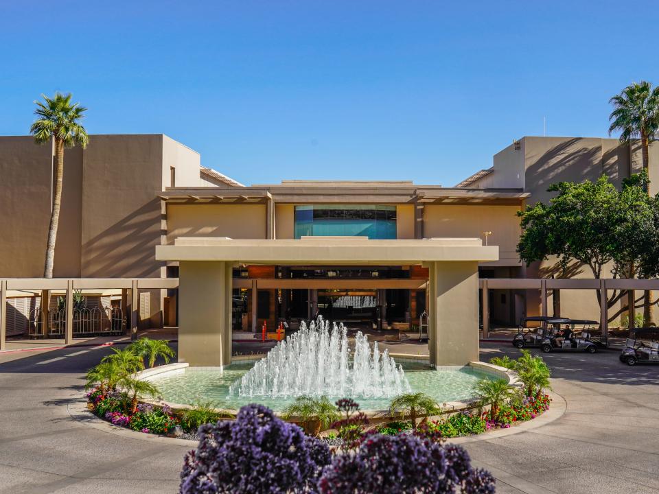 A boxy hotel entrance with a large, circular fountains out front and blue skies in the background