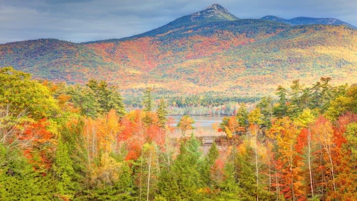 A lightly snowcapped Mount Chocarua rises above hills covered with foliage of reds, yellows and greens.