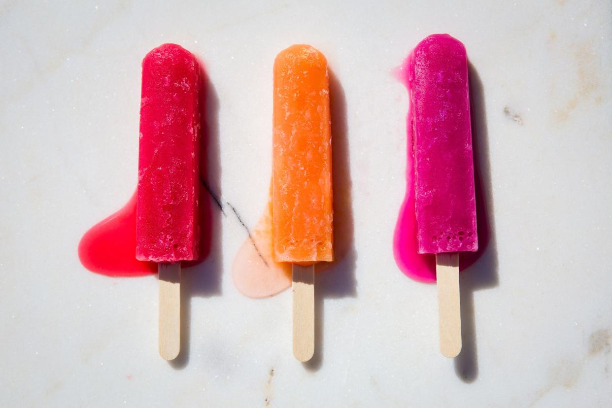 Red, orange, and pink popsicles slightly melting on a white marble slab