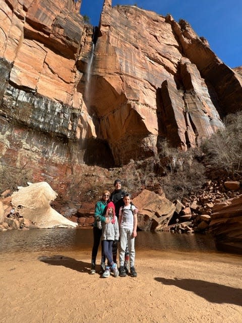 A family posing next to a red rock formation with a small waterfall.