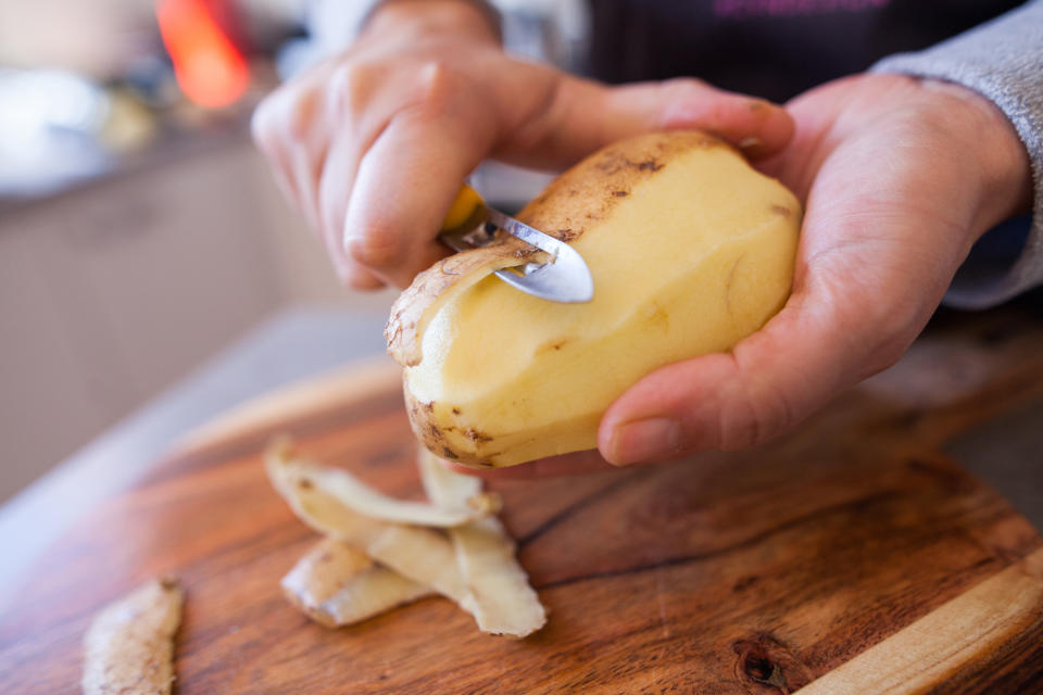 Person peeling a potato over a wooden cutting board