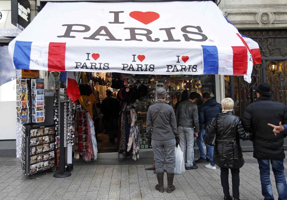 People stand in front of a tourist souvenir shop decorated with French national flags and the slogan "I love Paris" on the Champs Elysees Avenue in Paris, France, November 26, 2015. The French President called on all French citizens to hang the tricolour national flag from their windows on Friday to pay tribute to the victims of the Paris attacks. (REUTERS/Eric Gaillard)