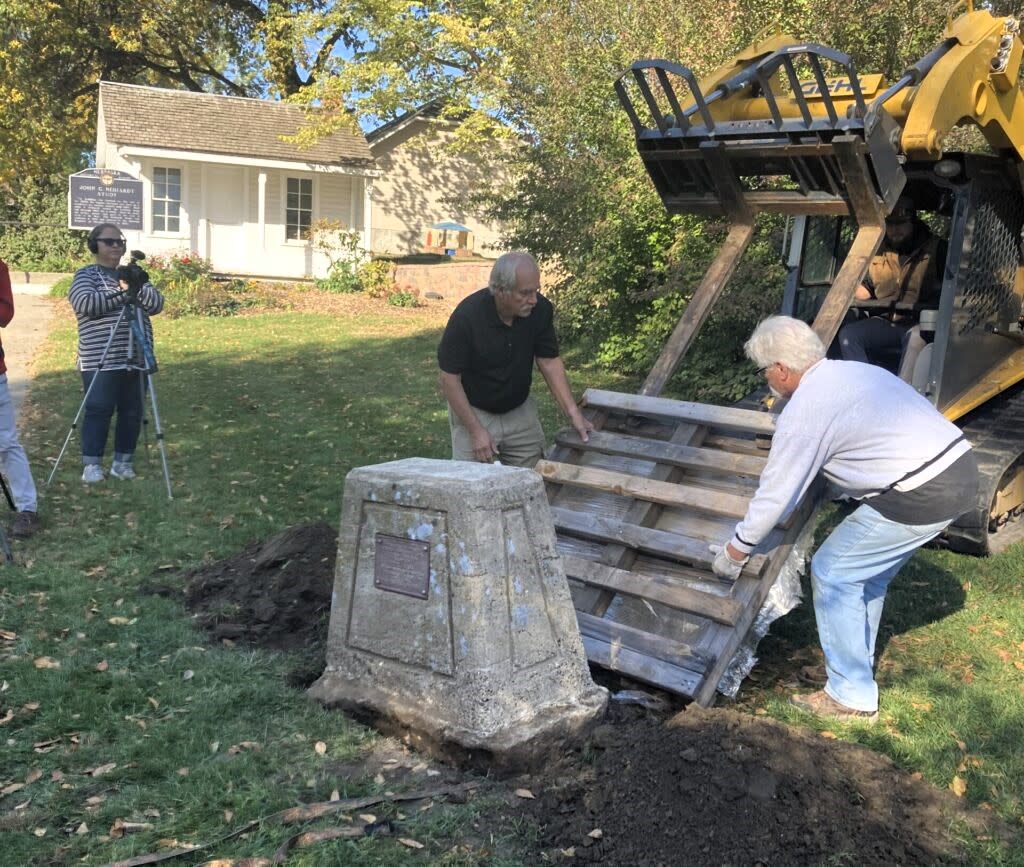 The descendants of poet/author John Neihardt work to ease a 3,200-pound monument into place at the state historic site dedicated to Neihardt. The study in the background is where Neihardt wrote “The Song of Hugh Glass,” the subject of the monument. (Paul Hammel/Nebraska Examiner)