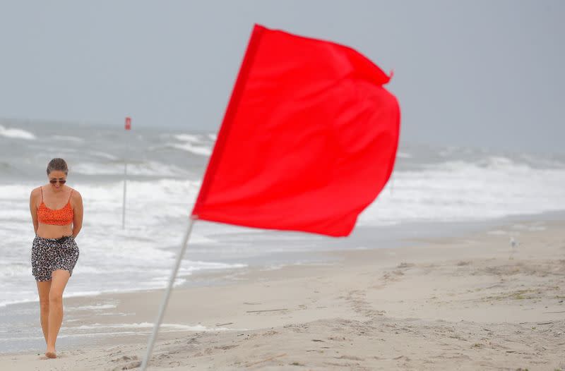 Una bandera de advertencia de tormenta ondea cuando una mujer camina por la playa antes del paso de la tormenta tropical Isaias en el área de Rockaway, en Queens, Nueva York