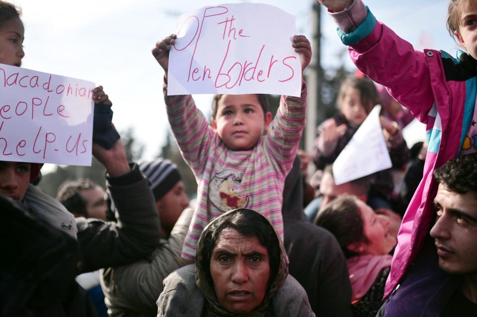 A child sits on a woman's shoulders and holds a sign that reads "Open the borders" at the makeshift camp in Idomeni. Migrants and refugees stuck near the border have staged daily protests condemning their desperate situation.&nbsp;