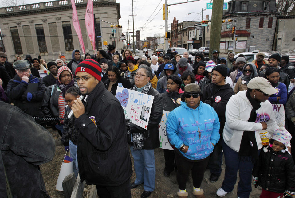 FILE - In this Feb. 13, 2011 file photo, Sean Brown, foreground left, of the Young Urban Leaders, uses a microphone to speak in Camden, N.J. at a rally remembering Anjanea Williams who died after she was hit by a stray bullet outside a nearby deli. Anjanea Williams' mother, Latonya Williams, is at center right, wearing sunglasses and a blue coat. A police reboot followed state budget cuts that had forced Camden to slash spending on police, libraries and other services in 2011. Nearly half of its 360 officers were laid off. Crime surged. Republican Gov. Chris Christie, along with local Democratic powerbroker George Norcross and others, engineered the plan to eliminate the police department, shed its costly union contract and create a county-run force. (AP Photo/Mel Evans, File)