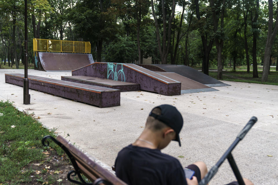 Rodion Kucherian, de 14 años, se toma un descanso en un parque vacío para mirar su celular en Kramatorsk, en la región de Donetsk, en el este de Ucrania, el miércoles 3 de agosto de 2022. Antes de la guerra, dijo, sus amigos y él hacían acrobacias en el popular parque junto a muchos otros niños. Pero ahora, su única conexión con sus amigos, que han huido a países como Polonia y Alemania, son los medios sociales. (AP Foto/David Goldman)