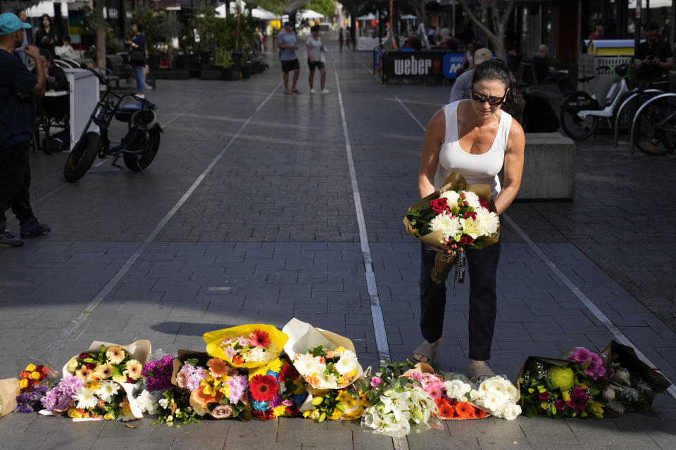 A woman brings flowers to an impromptu memorial at Bondi Junction in Sydney, Sunday, April 14, 2024, after several people were stabbed to death at a shopping center a day earlier. (AP Photo/Rick Rycroft)