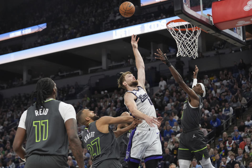 Sacramento Kings forward Domantas Sabonis, center, shoots from between Minnesota Timberwolves center Rudy Gobert and forward Jaden McDaniels, right, during the second half of an NBA basketball game Friday, March 1, 2024, in Minneapolis. (AP Photo/Abbie Parr)
