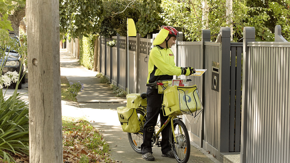 An Australia Post mailman delivering a letter from a bike. 