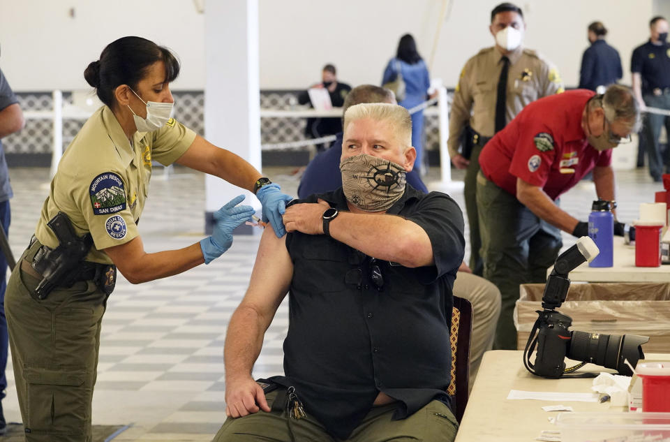 Los Angeles County Deputy Sheriff Photographer Ken Whitney, with the Scientific Services Bureau, is inoculated by Deputy Brod, left, COVID-19 mobile vaccination clinic for Sheriff's employees at the Pomona Fairplex in Pomona, Calif., Friday, March 5, 2021. More than 27 million Americans fully vaccinated against the coronavirus will have to keep waiting for guidance from U.S. health officials for what they should and shouldn't do. The Biden administration said Friday it's focused on getting the guidance right and accommodating emerging science. (AP Photo/Damian Dovarganes)