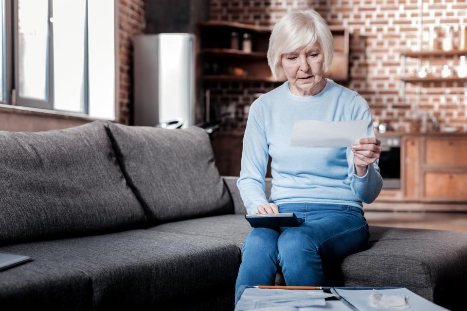 Senior woman sitting on couch looking at check with calculator.