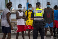 A police officer tells migrants and asylum-seekers to stop playing soccer due to coronavirus restrictions on contact sports in Gran Canaria island, Spain, Tuesday, Aug. 18, 2020. Migrants are increasingly crossing a treacherous part of the Atlantic Ocean to reach the Spanish archipelago near West Africa, in what has become one of the most dangerous routes to European territory. (AP Photo/Emilio Morenatti)