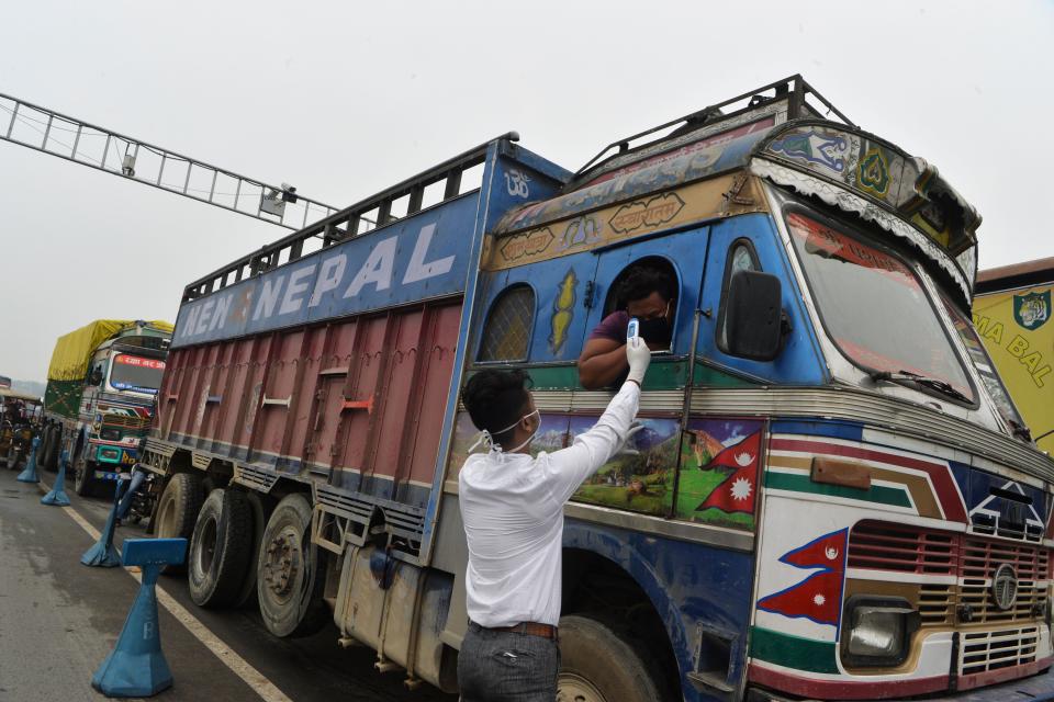 A member of medical staff wearing a facemask amid concerns over the spread of the COVID-19 checks the body temperature of a trucker arriving from Nepal at the India-Nepal border at Panitanki checkpoint, some 32kms from Siliguri.