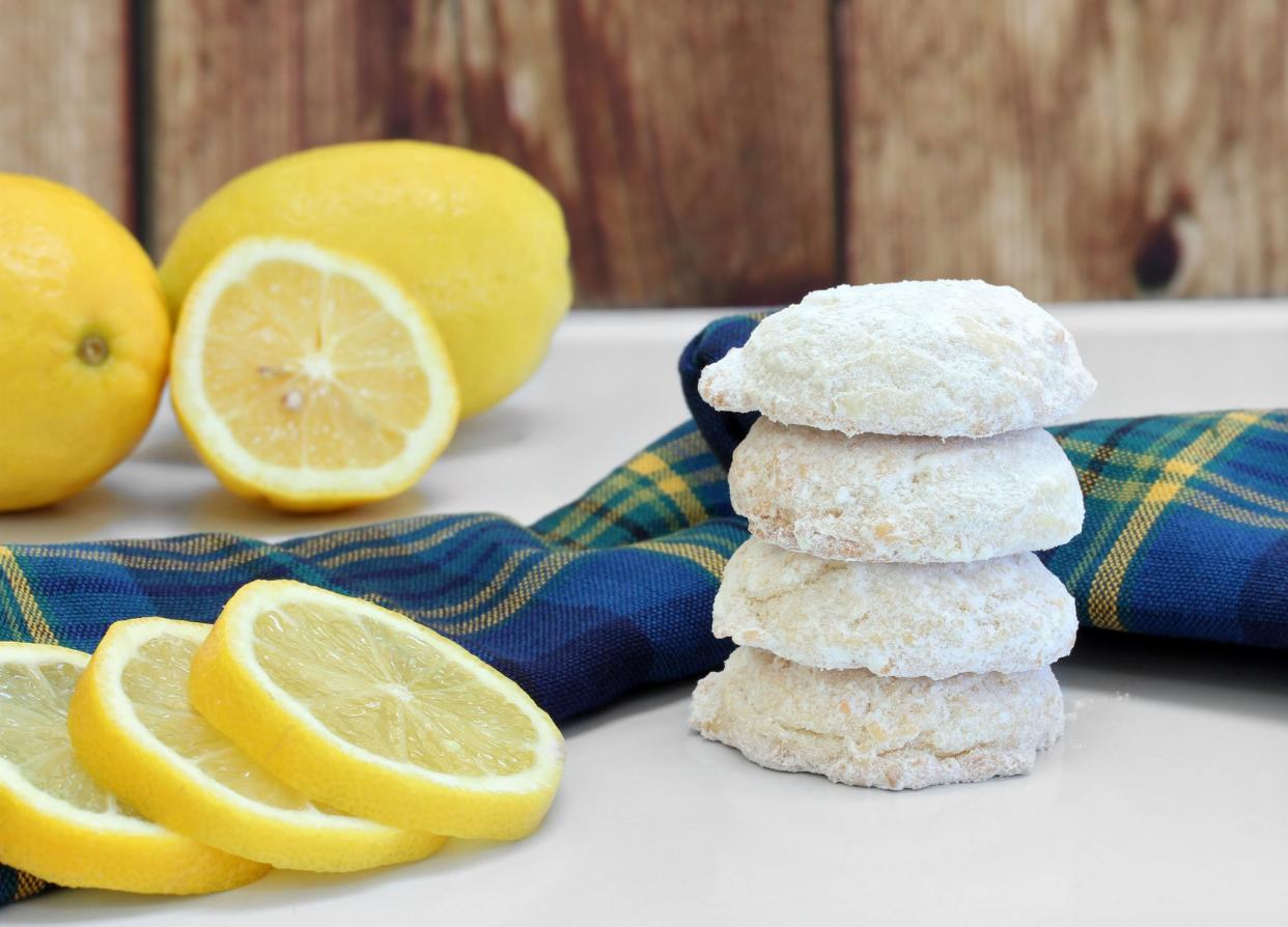 A stack of sugared lemon cookies, with whole and sliced lemons.