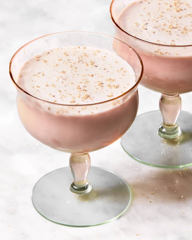 angled shot of two glasses of the pink squirrel cocktail on a marble surface, topped with shaved nutmeg.