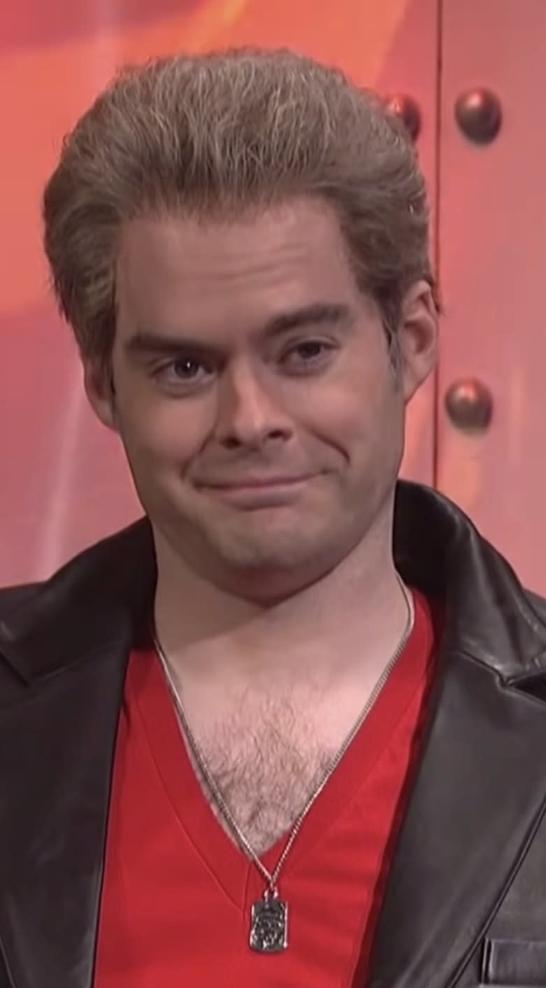 Hader wearing a wig, chain necklace, and leather jacket